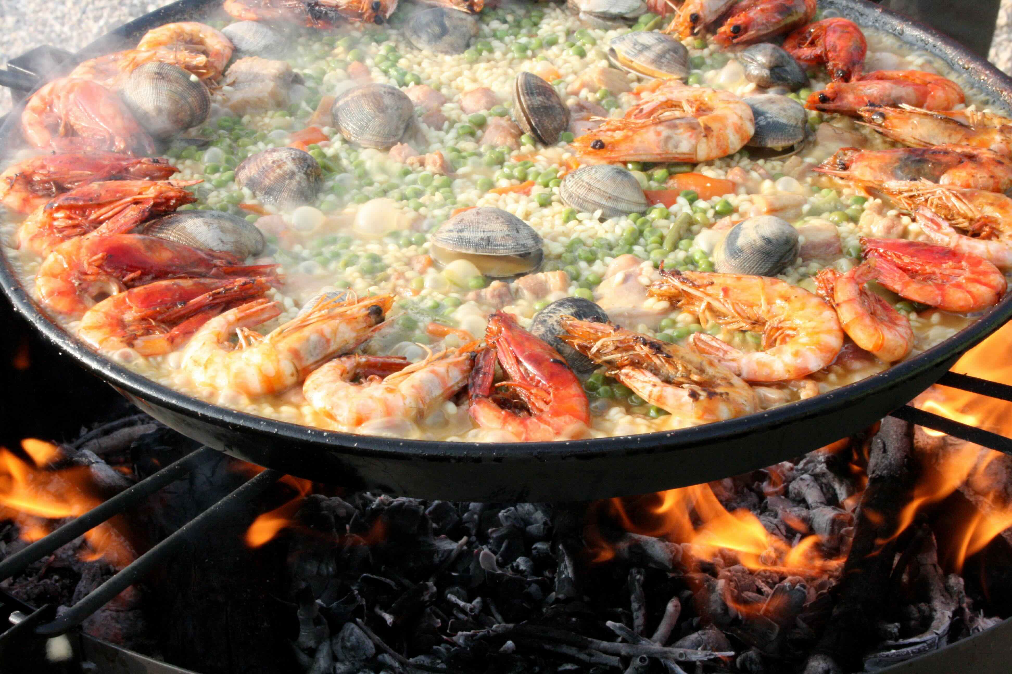 Paella Valenciana cooking over wood fire in a wide flat pan